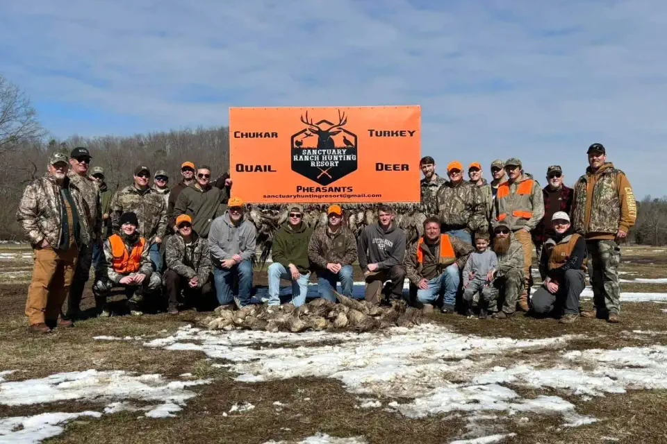 Group of hunters at The Sanctuary Ranch in Arkansas posing in front of lodge sign after a successful quail and pheasant hunt